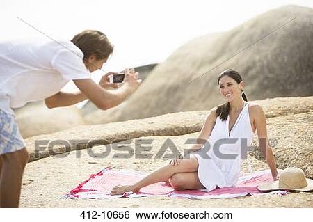 Stock Photograph - Man taking picture of girlfriend on beach. Fotosearch