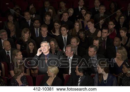 Stock Image - Man talking on cell phone in theater audience. Fotosearch