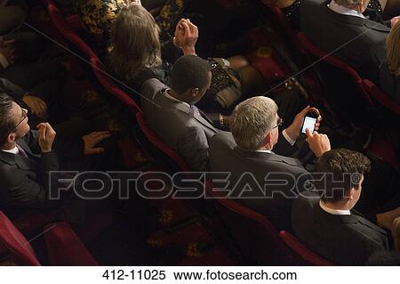 Stock Photography - Man using cell phone in theater audience. Fotosearch