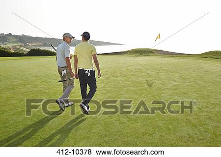 Stock Photo - Men walking toward hole on golf course overlooking ocean. Fotosearch