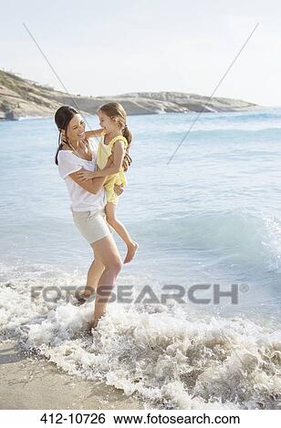 Stock Photograph - Mother and daughter playing in waves on beach. Fotosearch