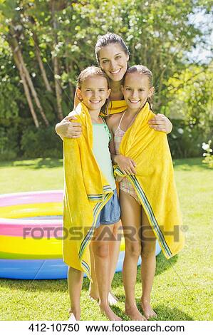 Stock Image - Mother wrapping daughters in towel in backyard. Fotosearch