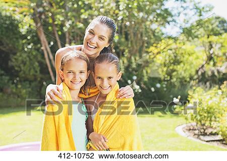 Stock Image - Mother wrapping daughters in towels in backyard. Fotosearch