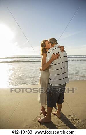 Stock Image - Older couple hugging on beach. Fotosearch