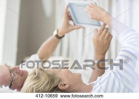 Stock Photo - Older couple using digital tablet on bed. Fotosearch