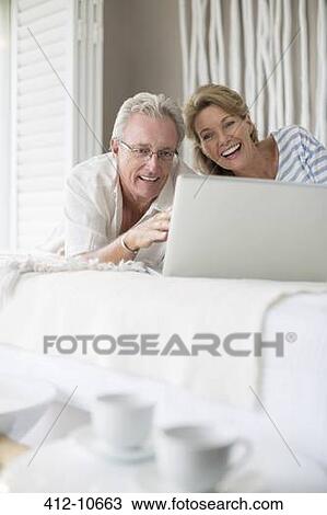 Older couple using laptop on bed View Large Photo Image Stock Image - Older couple using laptop on bed. Fotosearch