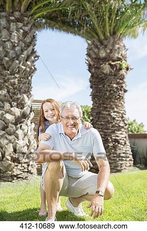Stock Photo - Older man and granddaughter smiling in backyard. Fotosearch