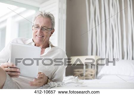 Stock Photo - Older man using digital tablet on bed. Fotosearch