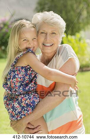Picture - Older woman holding granddaughter in backyard. Fotosearch