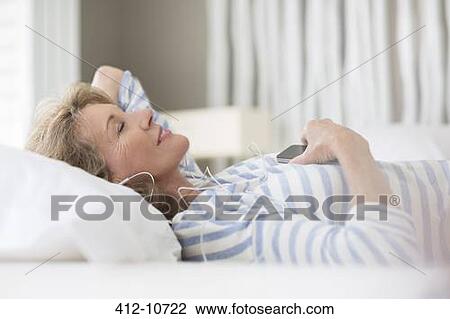 Older woman listening to earphones on bed View Large Photo Image Stock Image - Older woman listening to earphones on bed. Fotosearch