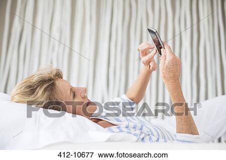 Older woman using cell phone on bed View Large Photo Image Stock Photo - Older woman using cell phone on bed. Fotosearch