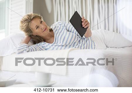 Stock Image - Older woman using digital tablet on bed. Fotosearch
