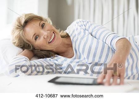 Stock Photo - Older woman using digital tablet on bed. Fotosearch