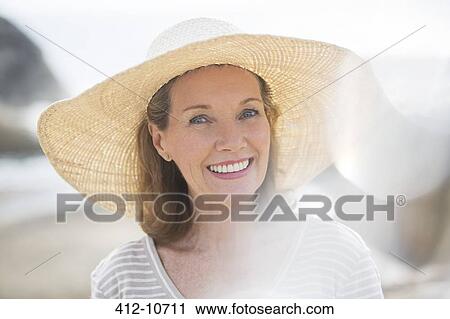Stock Image - Older woman wearing straw hat on beach. Fotosearch