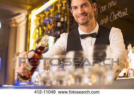 Stock Photo - Portrait of well dressed bartender pouring bourbon in luxury bar. Fotosearch