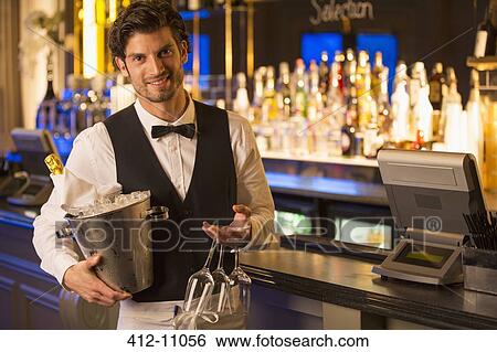 Stock Photograph - Portrait of well dressed bartender holding champagne bucket in luxury bar. Fotosearch