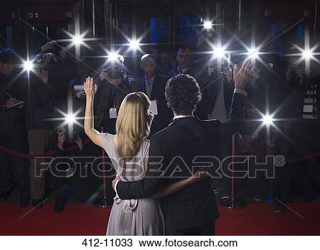Stock Image - Rear view of celebrity couple waving to paparazzi at red carpet event. Fotosearch