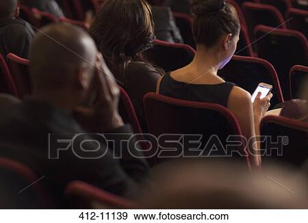 Rear view of woman using cell phone in theater audience View Large Photo Image Stock Photo - Rear view of woman using cell phone in theater audience. Fotosearch