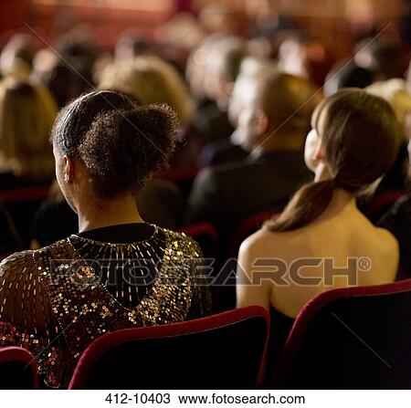 Stock Image - Rear view of women sitting in theater audience. Fotosearch