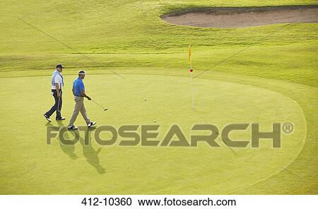 Stock Image - Senior men walking toward flag and hole on golf course. Fotosearch