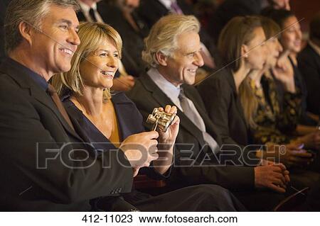 Stock Image - Smiling couple holding opera glasses in theater audience. Fotosearch