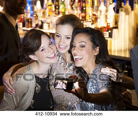 Picture - Smiling women hugging and taking self-portrait in nightclub. Fotosearch