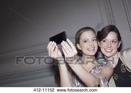 Stock Image - Smiling women taking self-portrait with camera phone. Fotosearch