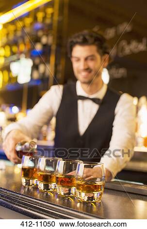 Stock Image - Well dressed bartender pouring bourbon in luxury bar. Fotosearch