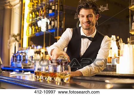 Stock Photo - Well dressed bartender pouring bourbon at luxury bar. Fotosearch