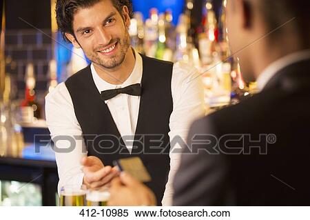 Well dressed bartender taking credit card from customer in luxury bar View Large Photo Image Stock Photography - Well dressed bartender taking credit card from customer in luxury bar. Fotosearch