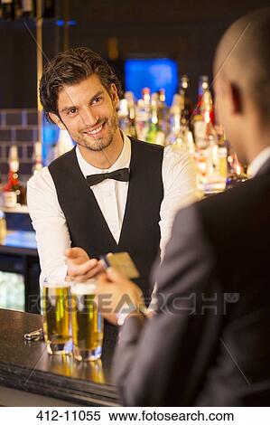 Stock Photography - Well dressed bartender taking credit card from customer in luxury bar. Fotosearch