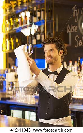 Stock Photo - Well dressed bartender wiping wine glass in luxury bar. Fotosearch