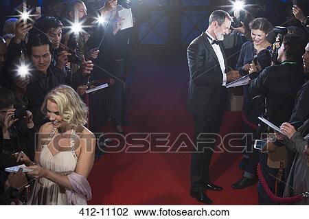 Stock Image - Well dressed celebrities signing autographs on red carpet. Fotosearch