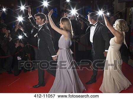 Stock Photo - Well dressed celebrity couples waving to paparazzi on red carpet. Fotosearch