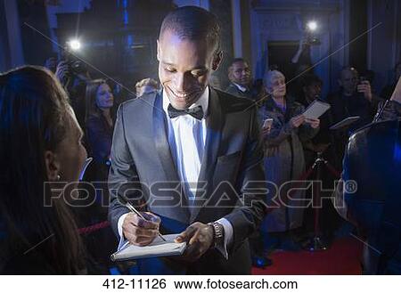 Stock Photograph - Well dressed celebrity signing autograph on red carpet. Fotosearch