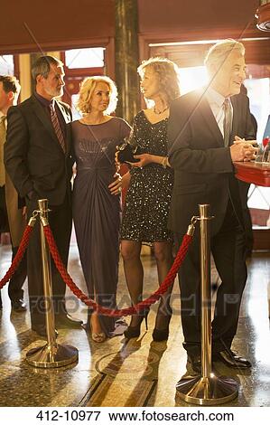 Stock Photo - Well dressed couples waiting in bar line in theater lobby. Fotosearch