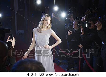 Stock Image - Well dressed female celebrity posing for paparazzi on red carpet. Fotosearch