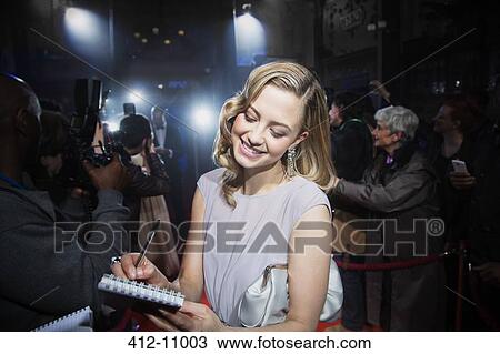 Stock Image - Well dressed female celebrity signing autographs at red carpet event. Fotosearch