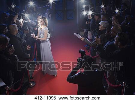 Stock Photography - Well dressed female celebrity signing autographs and posing for paparazzi on red carpet. Fotosearch