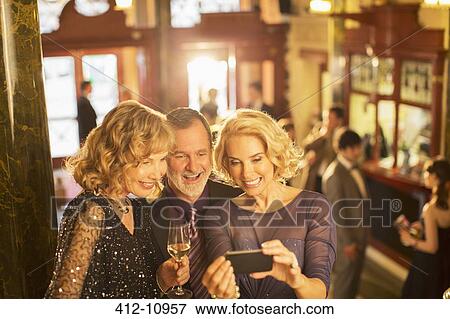 Stock Photo - Well dressed friends drinking champagne and looking at cell phone. Fotosearch