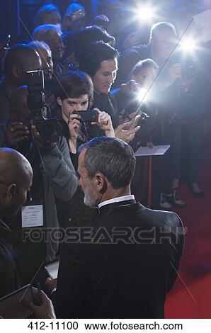 Stock Image - Well dressed male celebrity signing autographs at red carpet event. Fotosearch