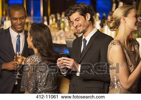 Well dressed man looking down at cell phone and smiling in luxury bar View Large Photo Image Stock Image - Well dressed man looking down at cell phone and smiling in luxury bar. Fotosearch