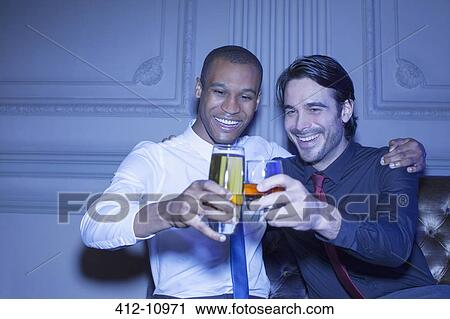 Stock Image - Well dressed men hugging and toasting beer and cocktail. Fotosearch