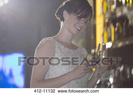 Stock Image - Well dressed woman with champagne looking down at cell phone. Fotosearch
