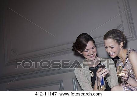 Well dressed women drinking champagne and looking at cell phone View Large Photo Image Stock Photo - Well dressed women drinking champagne and looking at cell phone. Fotosearch