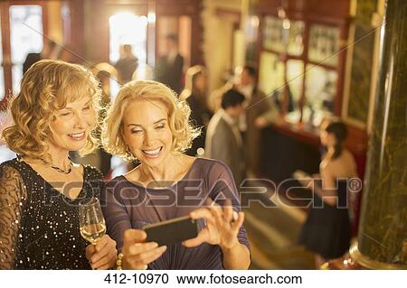 Well dressed women looking at cell phone in theater lobby View Large Photo Image Stock Image - Well dressed women looking at cell phone in theater lobby. Fotosearch