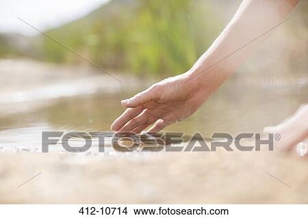 Picture - Woman dipping fingers in rural pond. Fotosearch