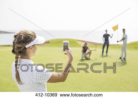 Woman photographing friends on golf course View Large Photo Image Stock Photo - Woman photographing friends on golf course. Fotosearch