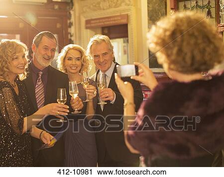 Woman photographing well dressed couples toasting champagne glasses in theater lobby View Large Photo Image Stock Image - Woman photographing well dressed couples toasting champagne glasses in theater lobby. Fotosearch