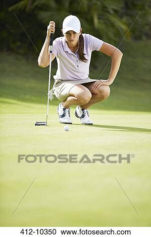 Stock Image - Woman preparing to putt on golf course. Fotosearch
